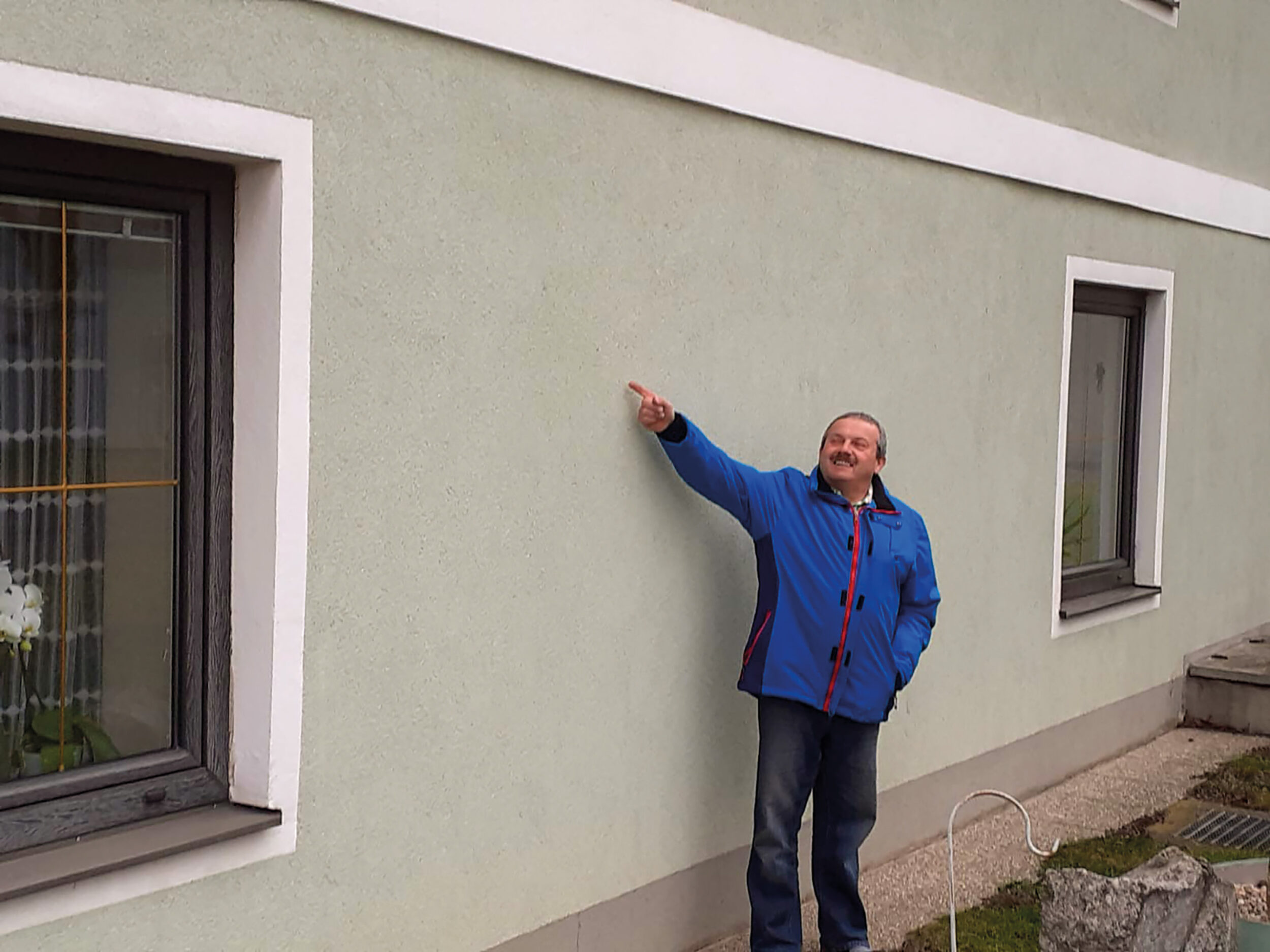 Herr Grenl zeigt die ehemalige Feuchteschadenshöhe an der Ostseite des Hauses an.